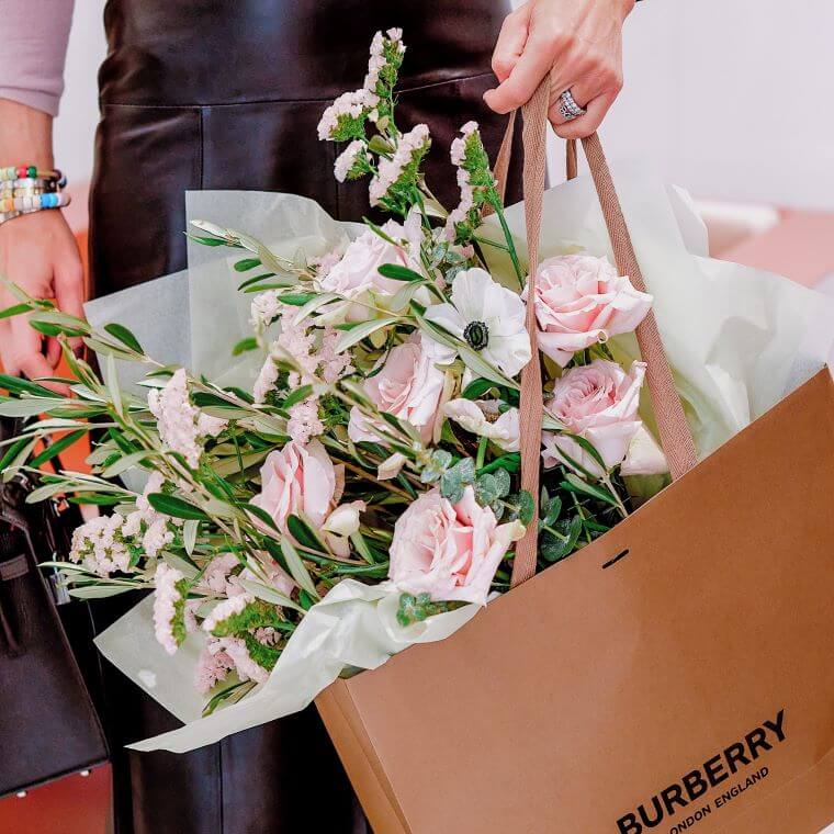 A hand carrying a bag containing pink and white flowers