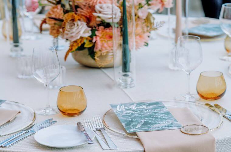 A table for an event set with crockery, cutlery, glassware, a menu, and a floral centrepiece