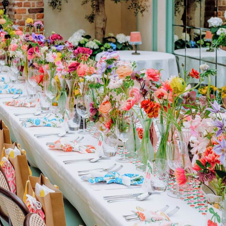 Long table set with multi-coloured flowers in many vases