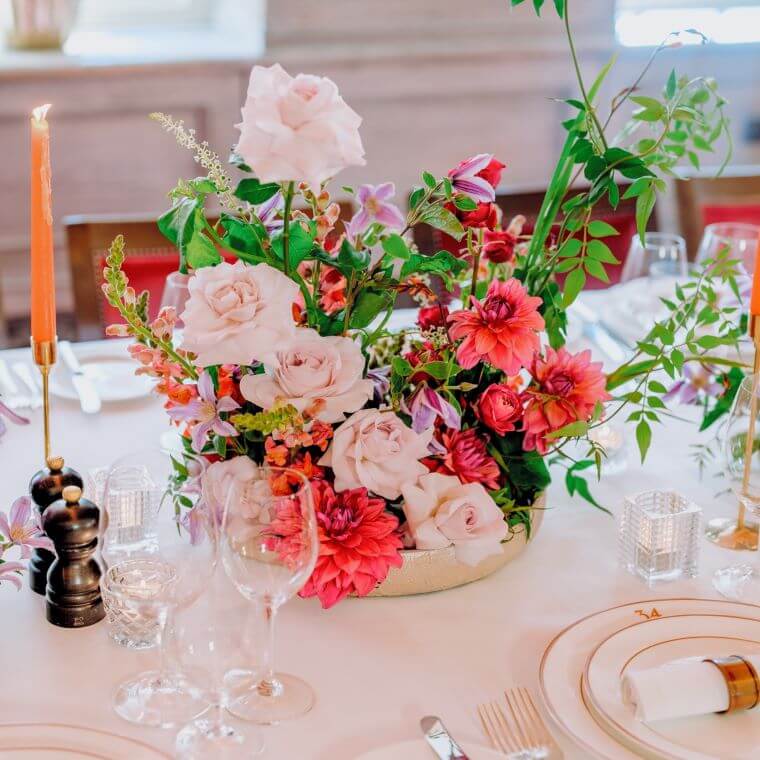 Pink and white flowers in a table centrepiece accompanied by candles and a table setting