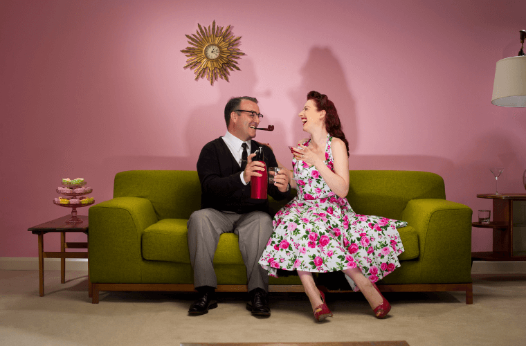 A man and woman sitting on a couch in the 1950s with the woman wearing a new look floral design dress