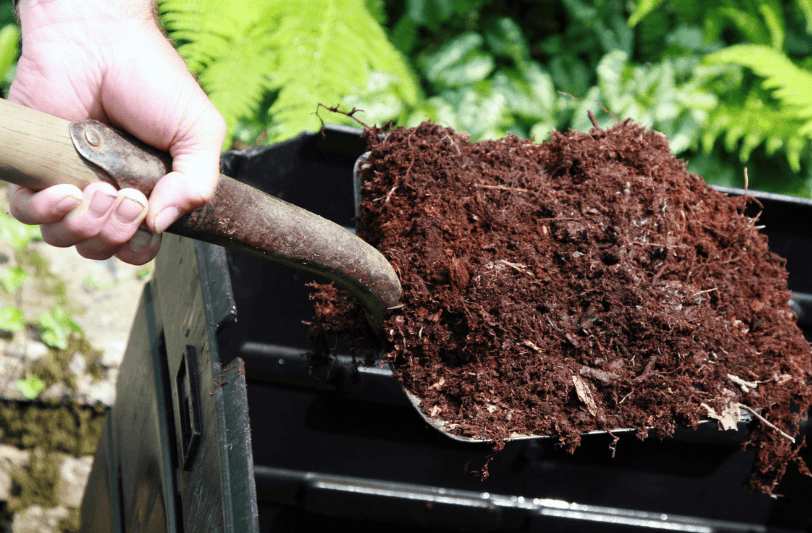 Hands holding a spade digging over compost in a bin