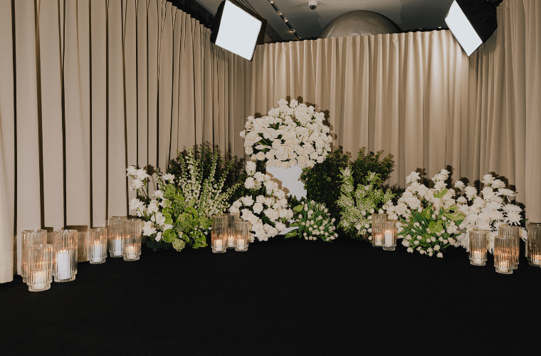 White and green floral display in front of beige curtains with a dark floor