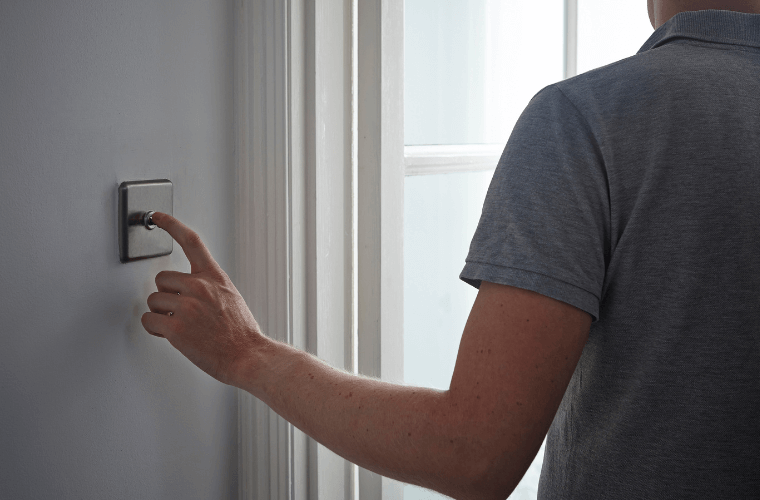 A man with his back to the camera switching off a light switch