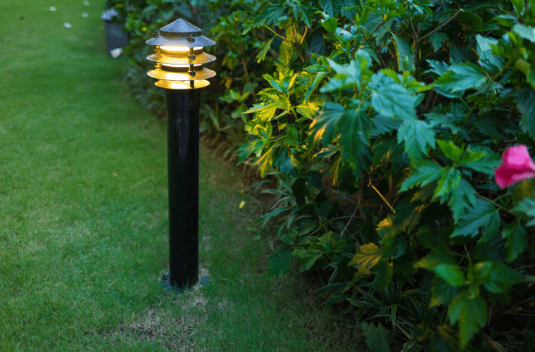 A garden light on a short pole next to plants