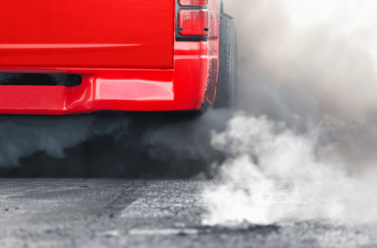 Part of a red car with the exhaust emitting fumes
