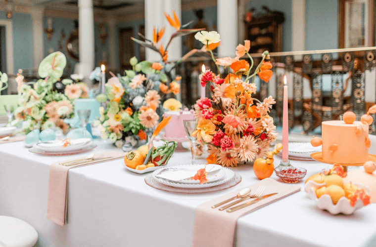 A wedding table set with flowers, candles, and cake in shades of apricot, yellow, and green