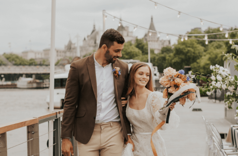 A wedding couple walking by a river with the bride holding a bouquet