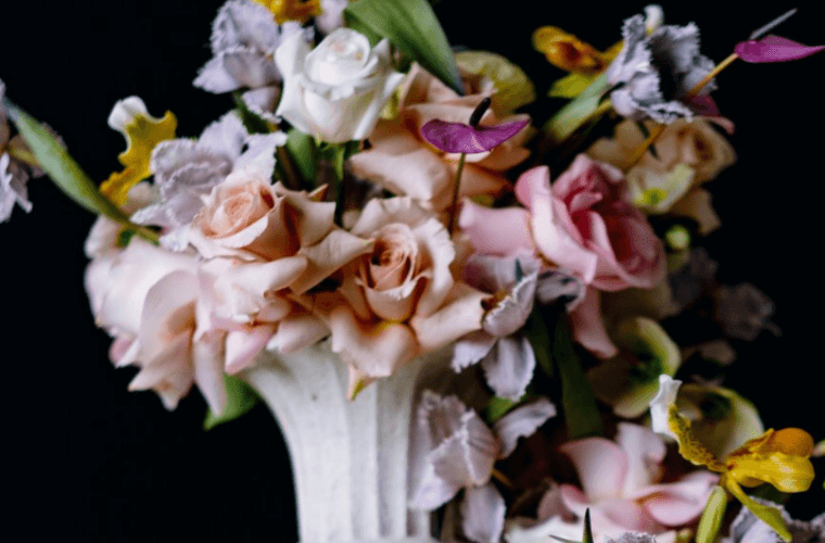 A vase with a display of flowers in pastel colours mainly featuring roses