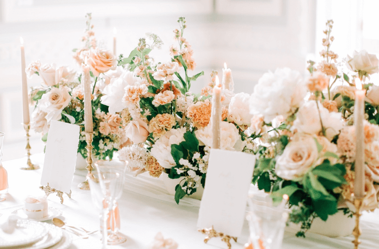 A wedding table set up with peach and mint coloured flowers, candles, and place settings