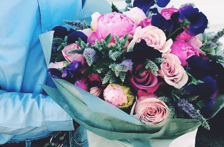 A man's hand carrying a bouquet with flowers of fuchsia, teal, pink, and peach