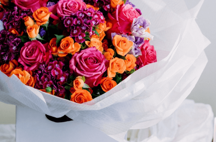 A bouquet of flowers in red, pink, orange, and purple mostly consisting of roses