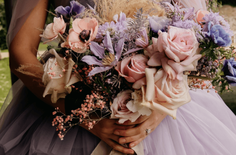 A bride's hands holding a bouquet with lilac, lavender, and pink coloured flowers