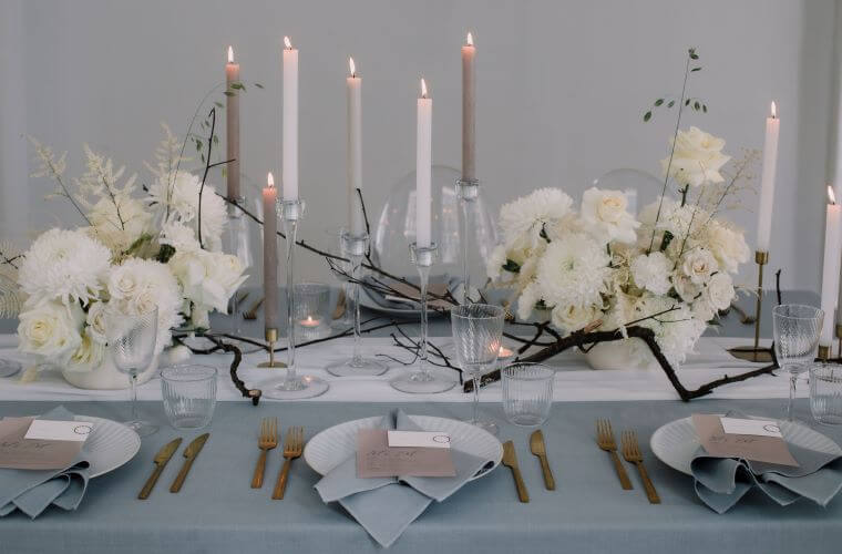 A table set with white flowers candles and place settings for a celebration