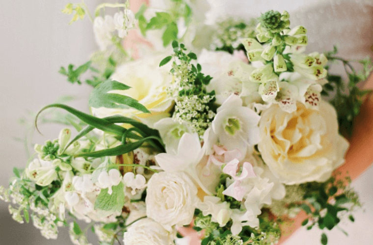 Female hands holding a bouquet of white and gold flowers with green foliage