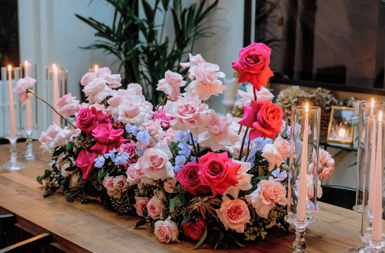 Pale pink and dark pink roses with green foliage on a table with candles