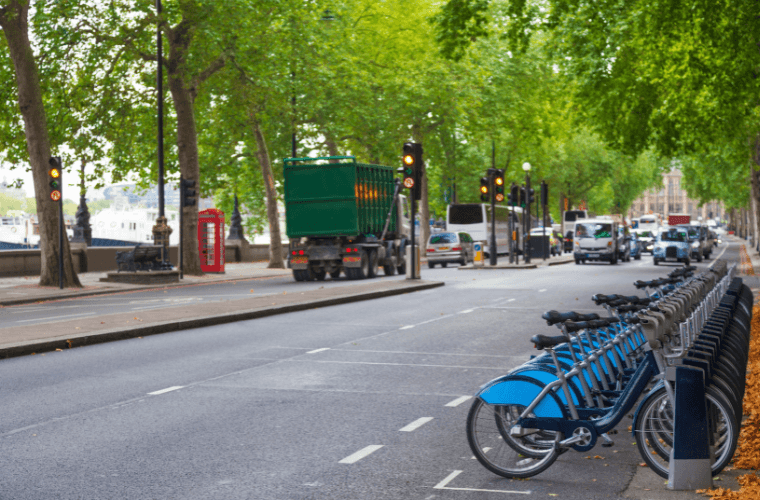 A street in london next to the thames with trees and a line of bikes to hire