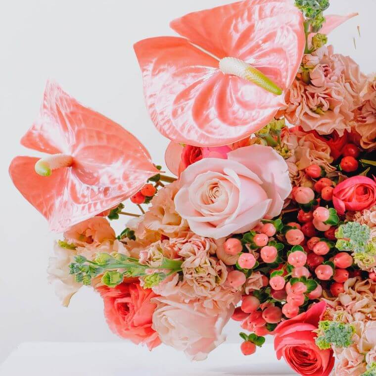 A bouquet of flowers in different shades of pink including pink avalanches roses and peach anthuriums