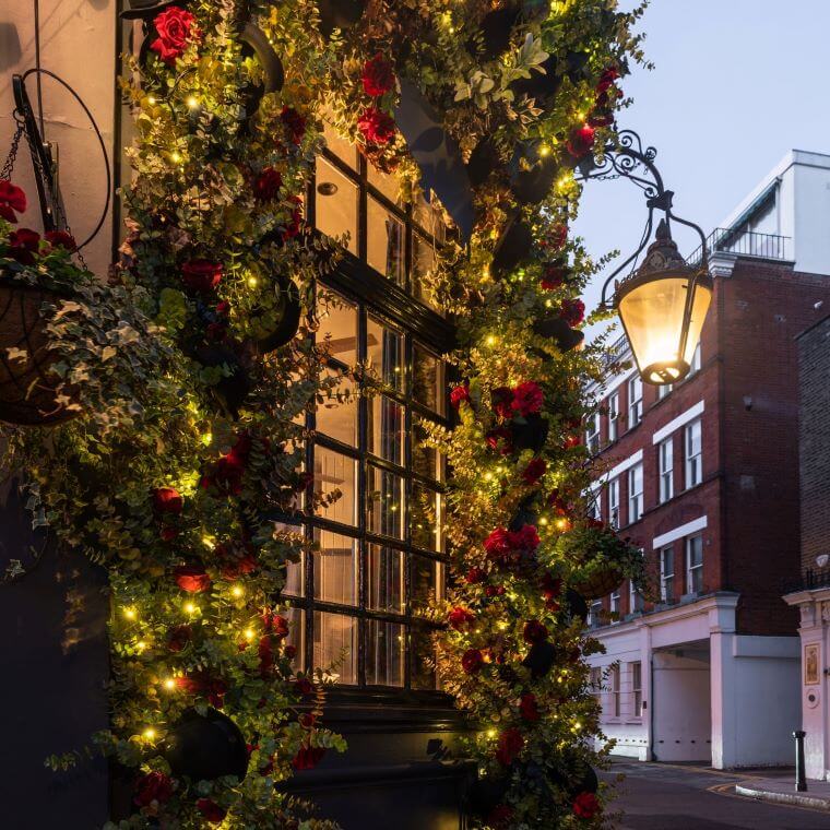 An arch of flowers an greenery around a window with small bright lights added