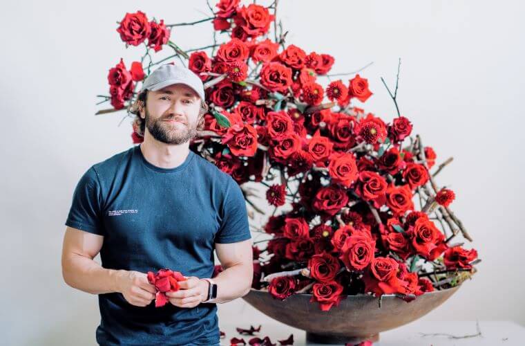 Master florist michal standing beside his sustainable design created with red roses