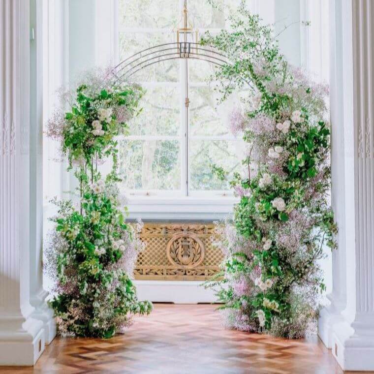 A white and green flower arch in a doorway with a window in the background