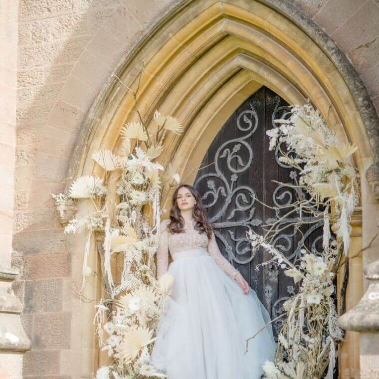 Bride with a white wedding arch in front of an arched church window