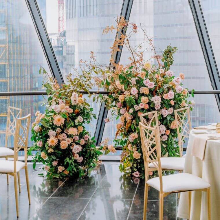 A small decorative flower arch with roses and dahlia in front of a window