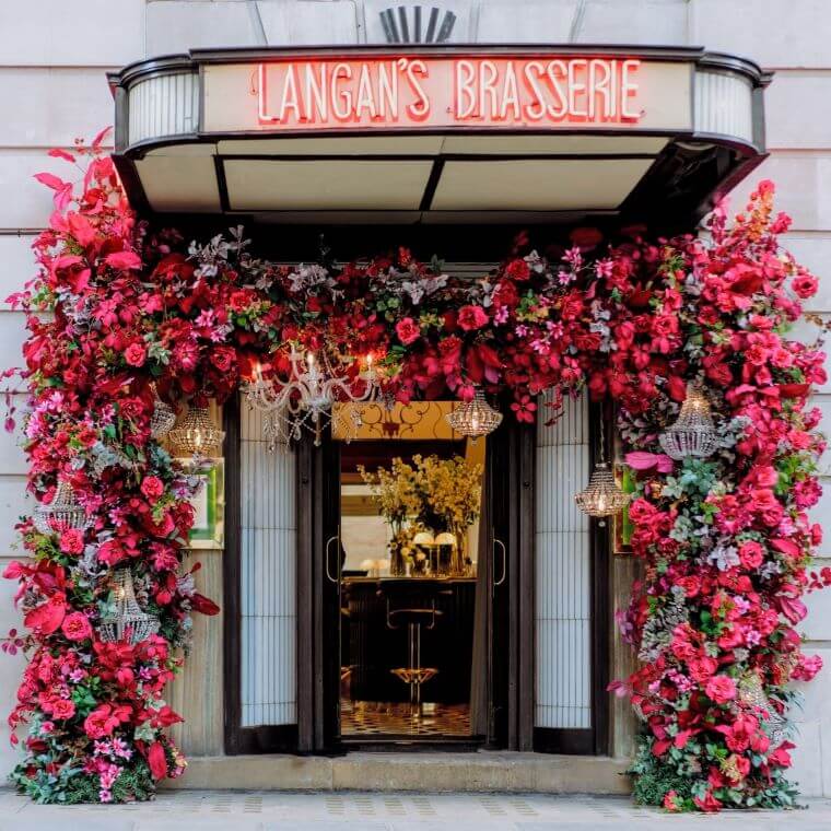 A flower arch with red blooms at the entrance to langan's  brasserie