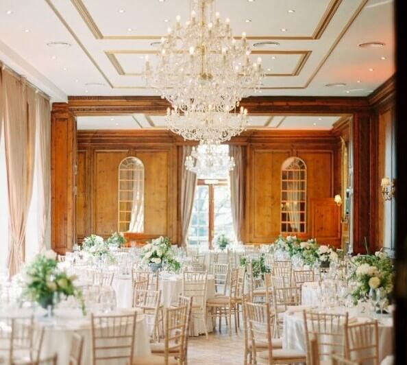 A large room set out with several tables decorated for a wedding and featuring white and green floral displays