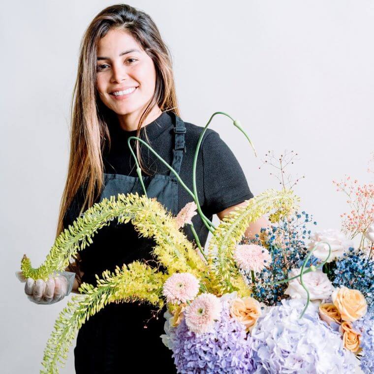 A female florist displaying a floral design created using pastel coloured flowers