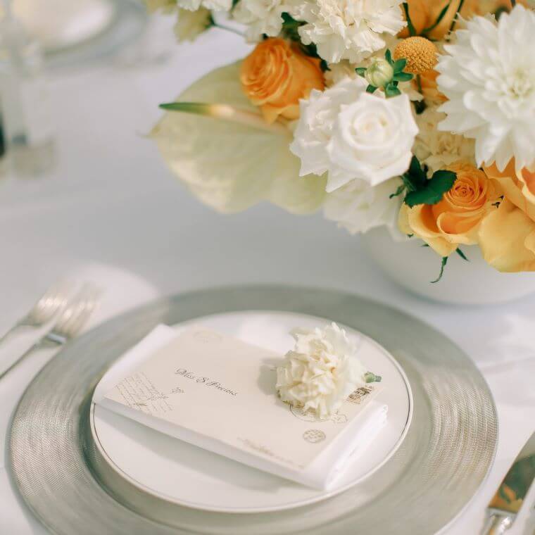 A silver and white wedding place setting with white and gold flowers