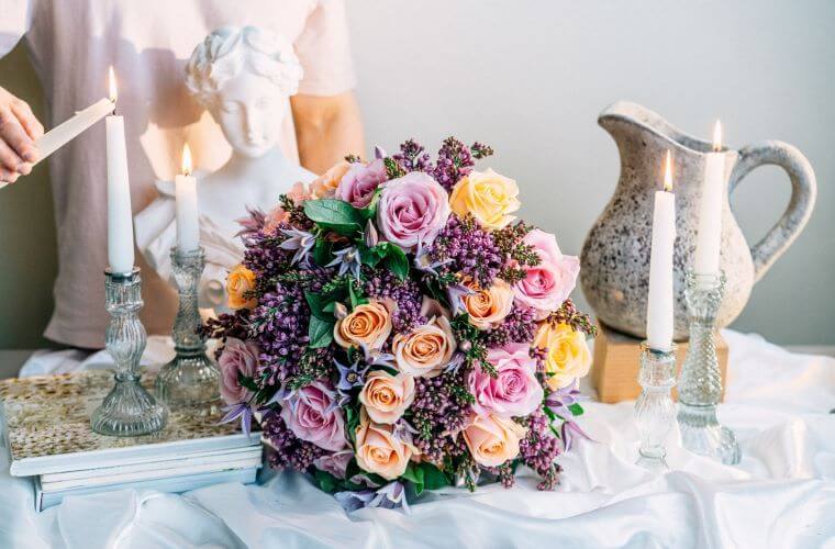 A florist lighting a candle on a table landscape that contains a floral arrangement with peach and pink roses