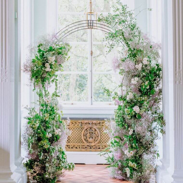 A wedding arch with green foliage and white flowers in front of a window