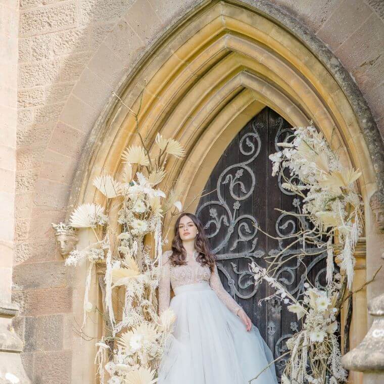 A bride surrounded by a white flower installation with a church arch as a backdrop