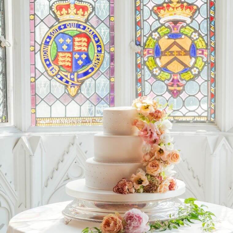 A three-tier wedding cake decorated with flowers cascading towards the table