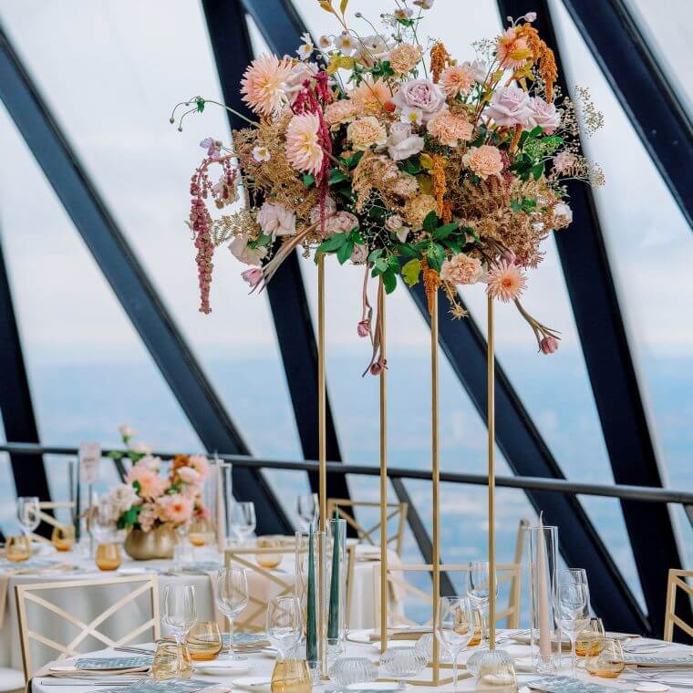 Table centrepiece of  flowers in pastel shades elevated off the table so guests can see each other below the display