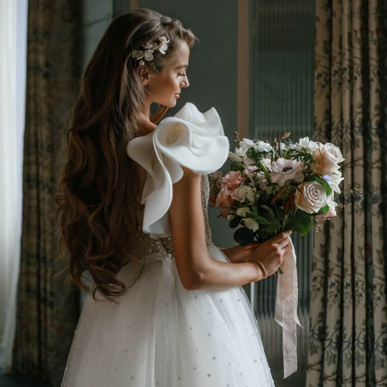 A side view of a young bride holding a bouquet of pink and cream flowers