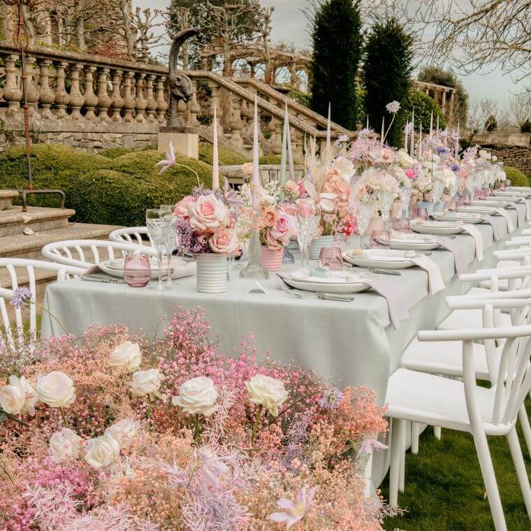 A wedding table in an outdoor setting decorated with flowers in shades of pink, peach, cream, and white including roses