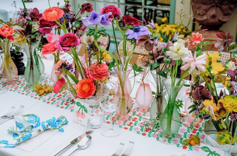 A selection of vases containing brightly coloured flowers decorating a table top