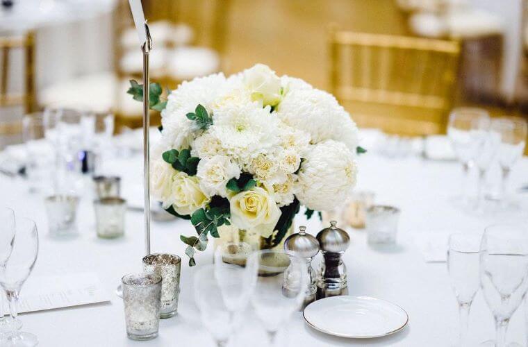 Votives used around a white rose and dahlia table centrepiece