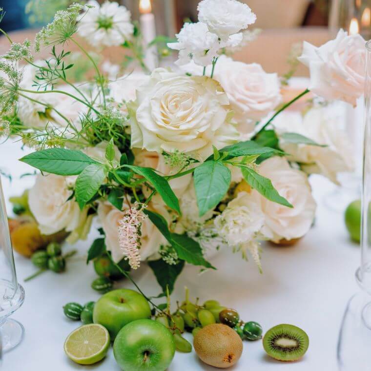 Pastel coloured floral display including items of fruit such as apples and kiwi fruit