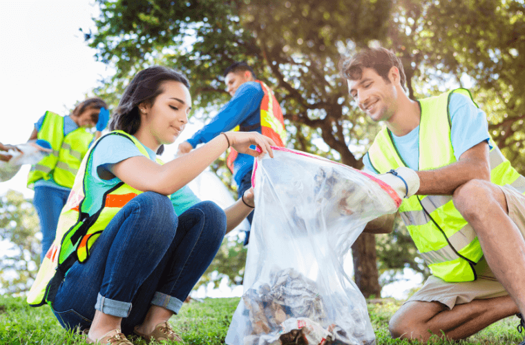 A man and a woman holding a bag and collecting rubbish with another man and woman in the background