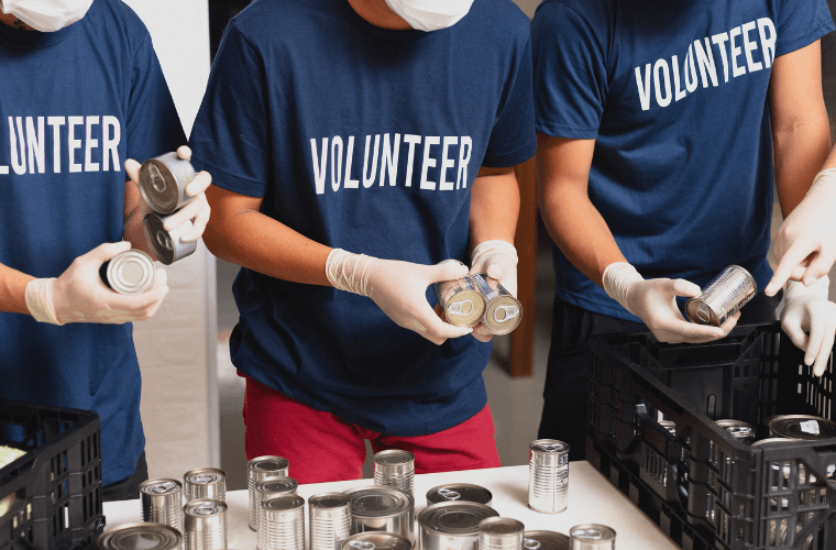 Three men wearing blue t-shirts with the word volunteer on them labelling cans