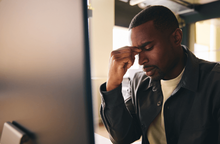 A man holding the bridge of his nose as though he is feeling tense