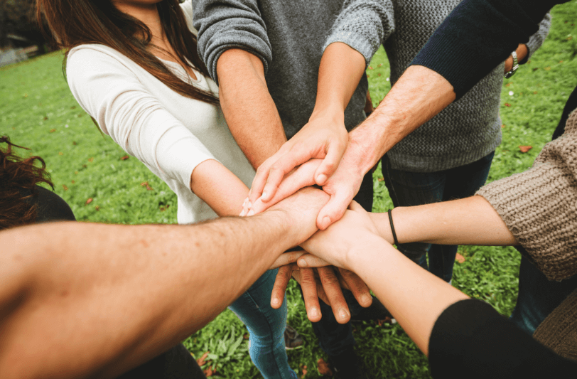 Seven people with one of their hands joined with all the others in the middle of a circle